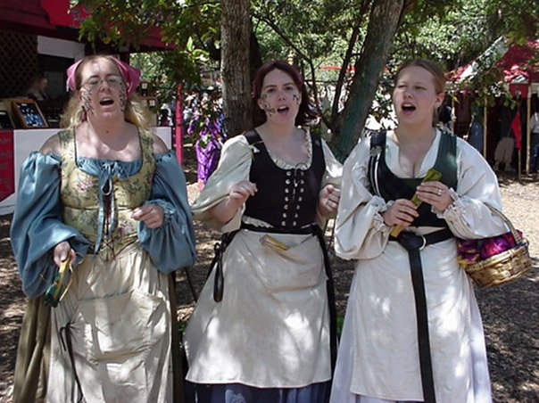 three young women dressed in renaissance peasant costumes singing