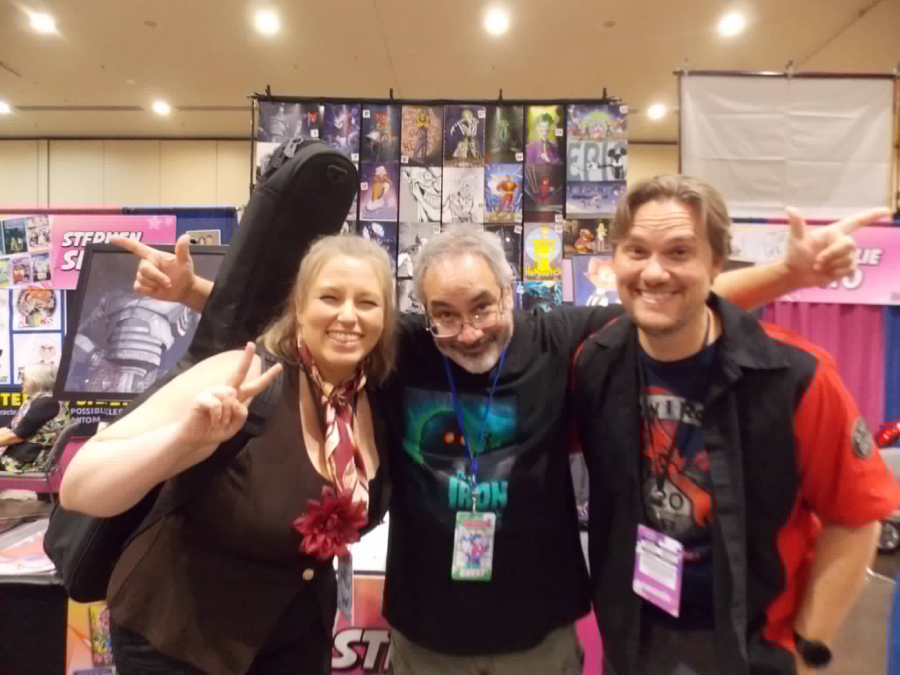a woman and two men smile while posing for a picture in front of an artist booth displaying prints at Animate Orlando 2026